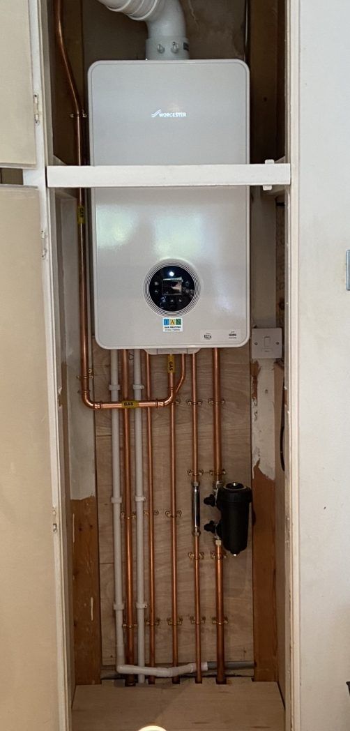 A new white Worcester Bosch 4000 boiler fitted in a lined-out airing cupboard, with copper pipework and a magnetic filter below