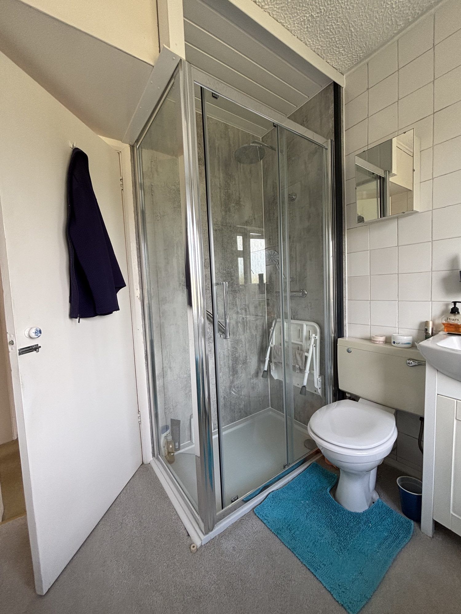 A new corner shower enclosure with grey wall panels, a fold-down seat and a grab rail, next to the toilet and basin