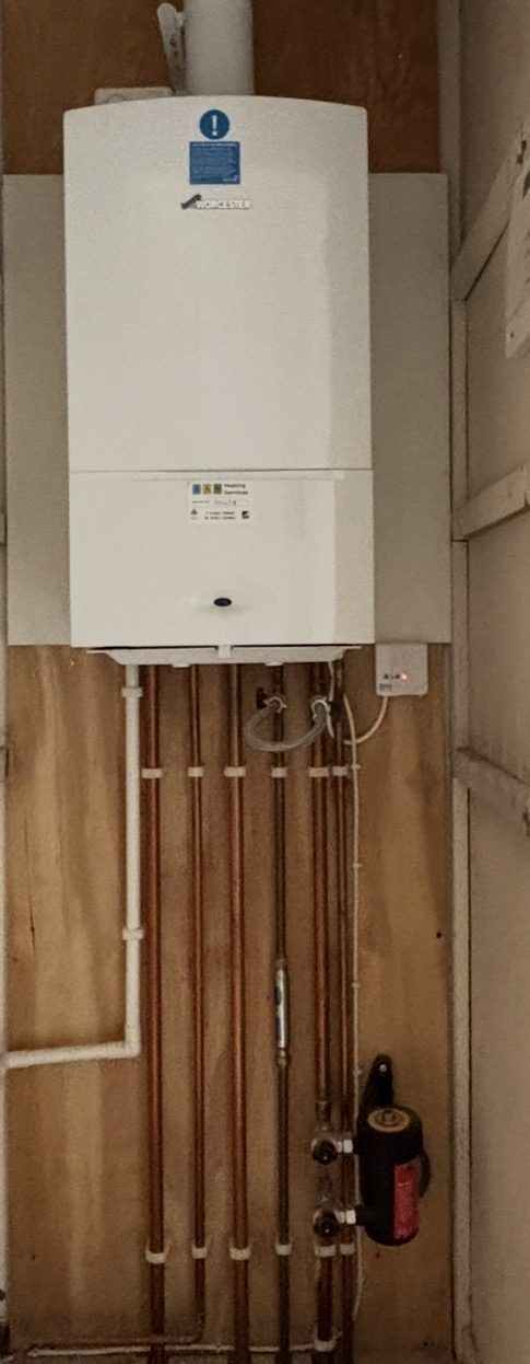 A white wall-hung Worcester Greenstar 24i boiler in a cupboard, with copper pipework and a magnetic filter below it