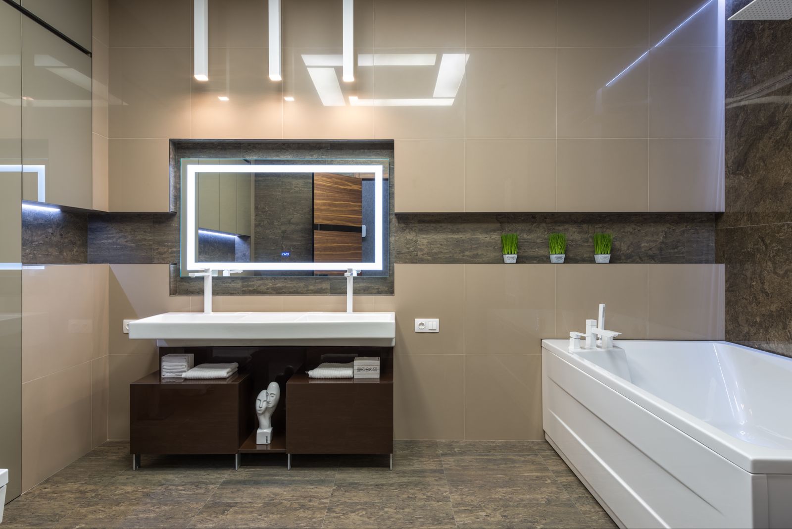 A white bath and basin in a light bathroom with a large mirror and grey tiles