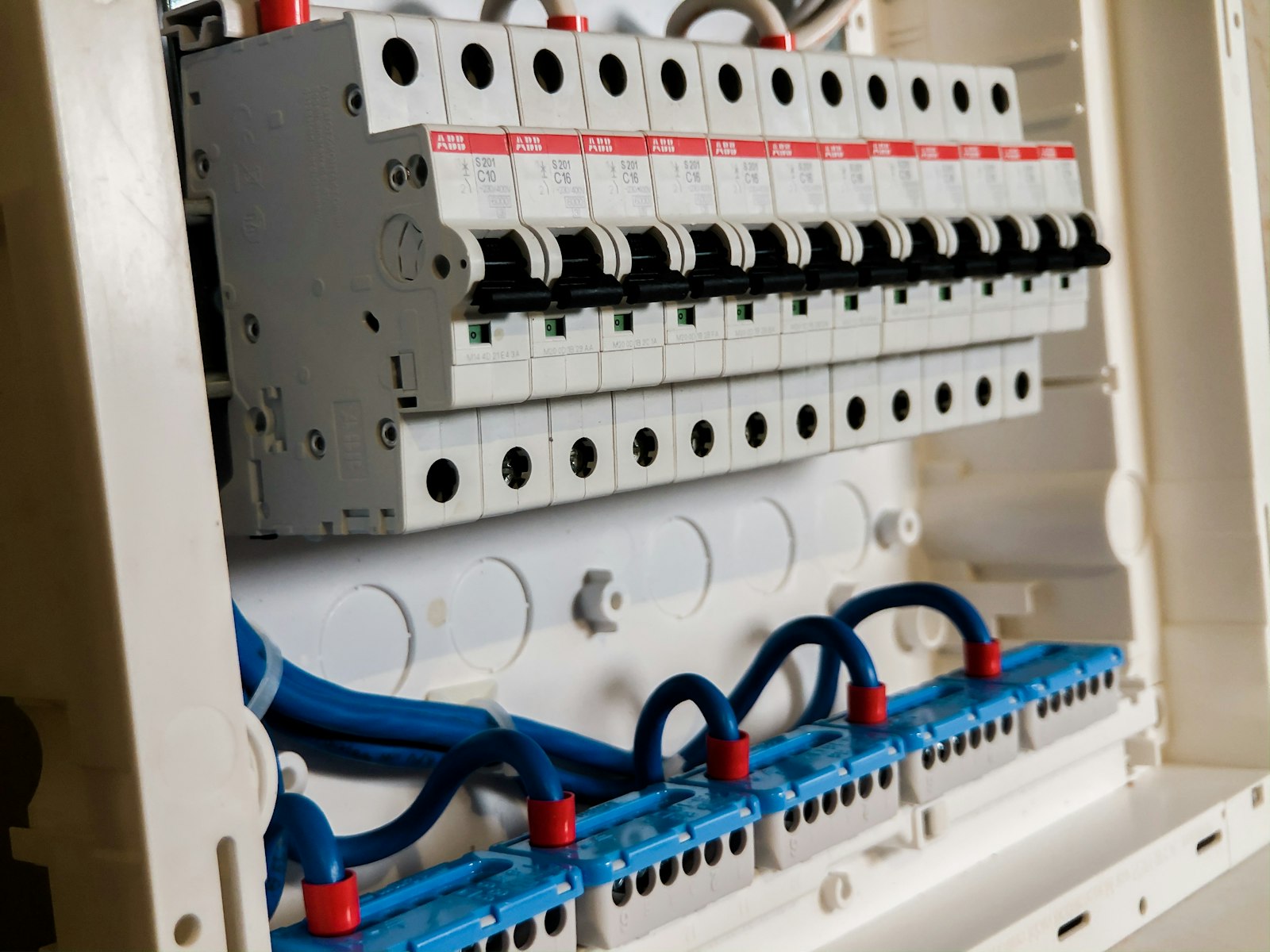 Rows of white circuit breakers in an open consumer unit with neat blue and grey wiring