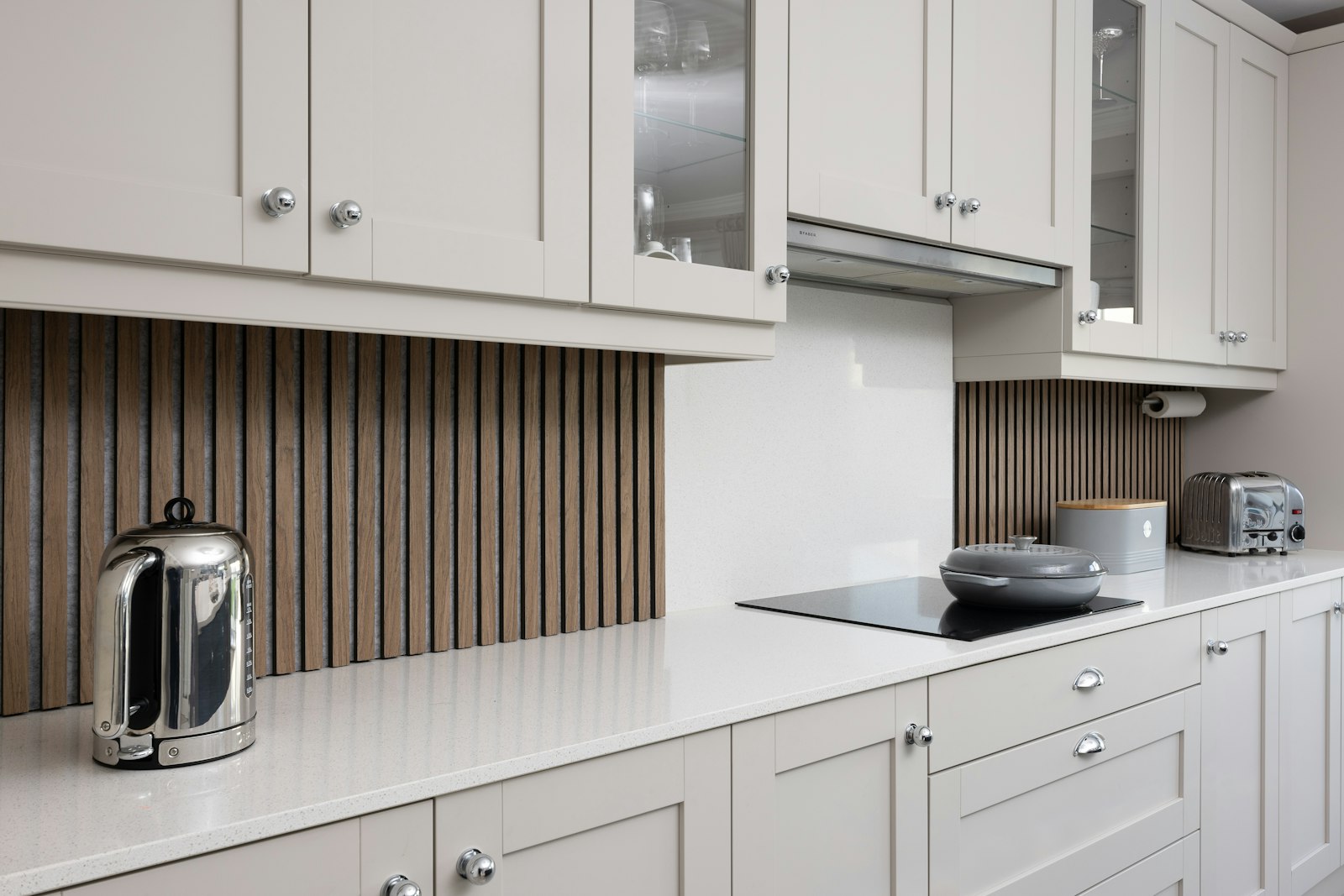 A white fitted kitchen with a built-in oven and hob, wooden worktop and dark splashback tiles