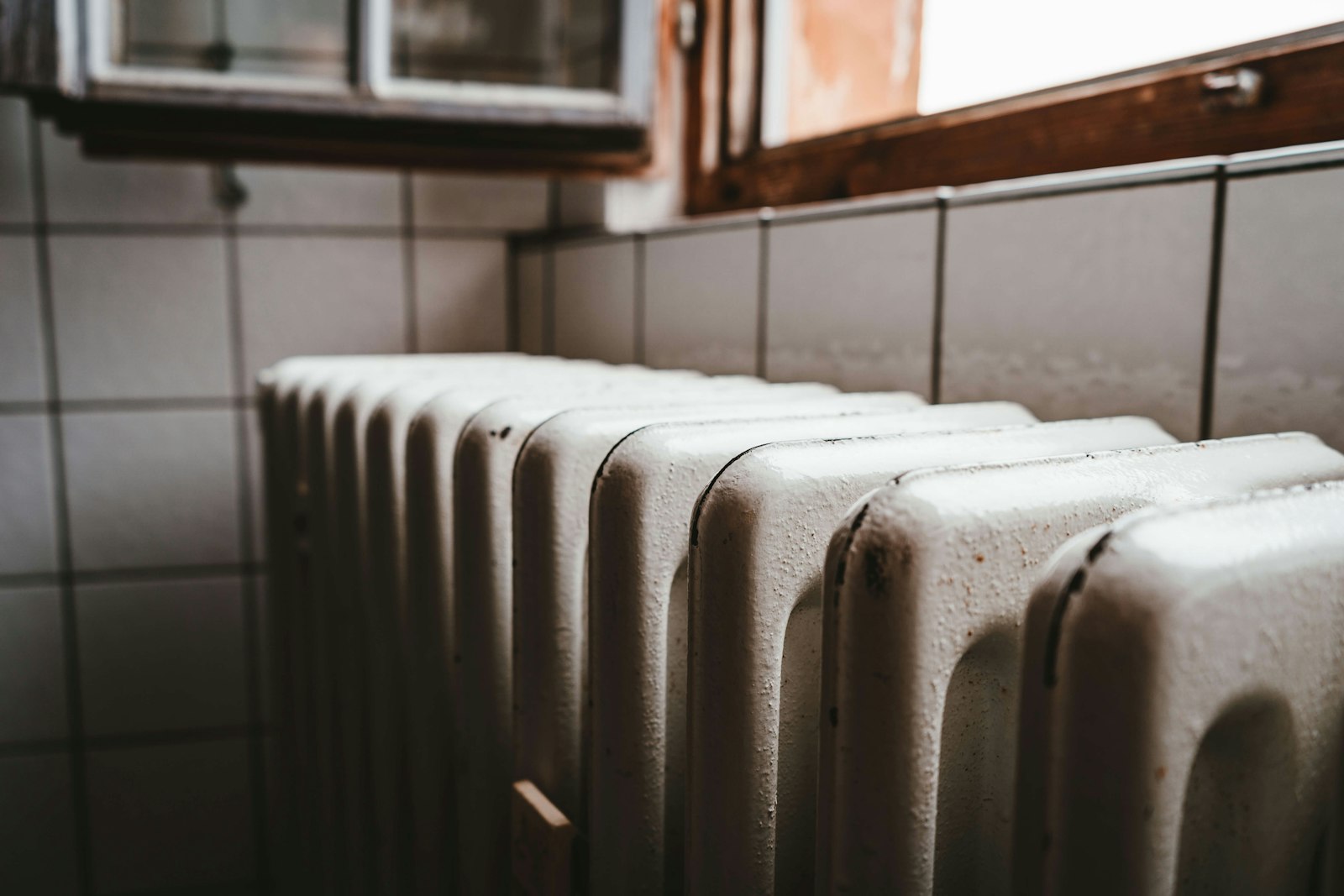 A white column radiator under a wooden-framed window in a plain room